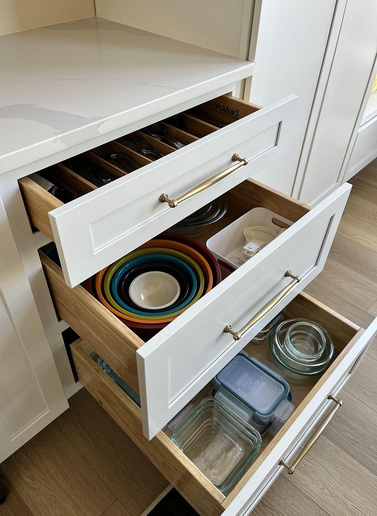 Open kitchen drawers organized with divider trays and glass containers